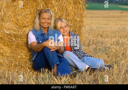 Madre e figlia in un campo appoggiata contro un round per balle di fieno Foto Stock