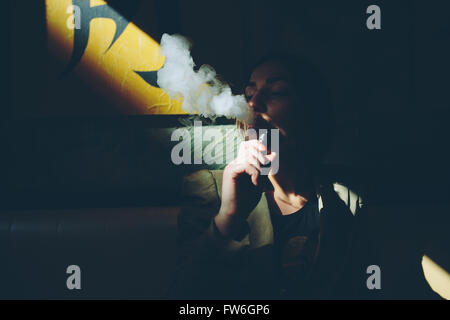 La ragazza si siede e fuma sigaretta elettronica Foto Stock