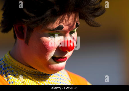 Clown faccia è un colorfully costituito da clown con un luminoso naso rosso scuro e capelli ricci in cerca di festa. Foto Stock