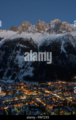 Resort di montagna di notte dominato da alte cime frastagliate. Aguilles (Needles) de Chamonix, Haute-Savoie, Auvergne-Rhône-Alpes, Francia. Foto Stock