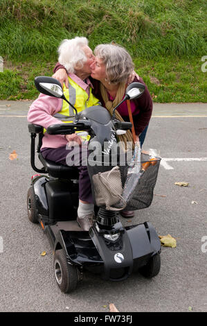 Donna anziana seduto nel suo scooter di mobilità baciando e abbracciando il suo caregiver Foto Stock