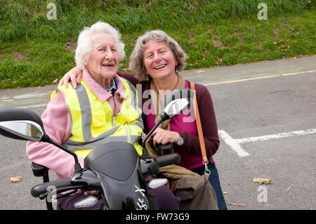 Ritratto di una donna anziana seduto nel suo scooter di mobilità con il suo caregiver Foto Stock