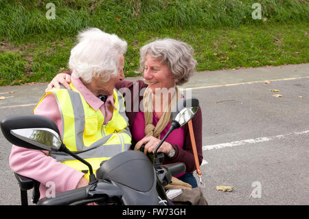 Donna anziana seduto nel suo scooter di mobilità a parlare con il suo caregiver Foto Stock