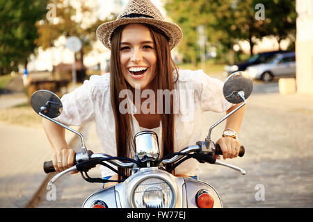 Ritratto di una bella ragazza seduta in argento scooter retrò, sorridente e guardando la telecamera Foto Stock