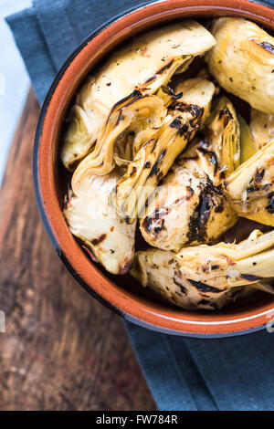 Chargrilled carciofi in vaso di ceramica, dal di sopra sulla tavola di legno. Foto Stock