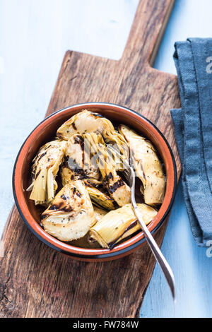 Chargrilled carciofi in vaso di ceramica, dal di sopra sulla tavola di legno. Foto Stock