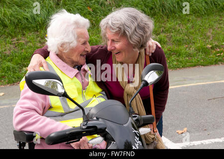 Donna anziana seduto nel suo scooter di mobilità a parlare con il suo caregiver Foto Stock