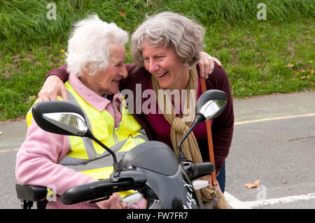 Donna anziana seduto nel suo scooter di mobilità a parlare con il suo caregiver Foto Stock