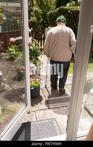 Vista posteriore di un anziano uomo che cammina con due bastoni da passeggio nel suo giardino Foto Stock