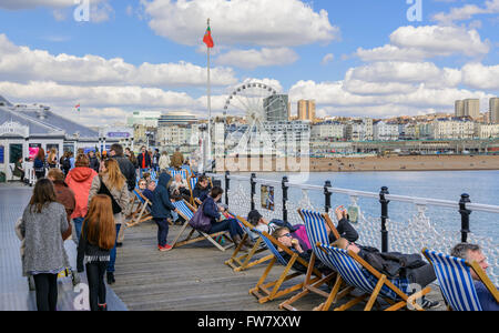 La gente camminare e seduti in sedie a sdraio sul molo di Brighton a Brighton, Brighton & Hove, East Sussex, Inghilterra, Regno Unito. Foto Stock