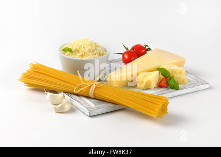 Parmigiano fresco, verdure guarnire e fascio di materie spaghetti sul tagliere di legno Foto Stock