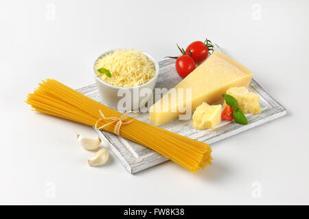 Parmigiano fresco, verdure guarnire e fascio di materie spaghetti sul tagliere di legno Foto Stock