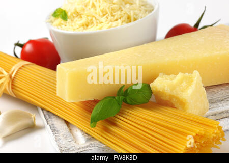 Dettaglio del parmigiano fresco, verdure guarnire e fascio di materie spaghetti sul tagliere di legno Foto Stock