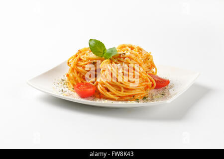 Piatto di spaghetti cotti con pesto rosso e parmigiano grattugiato su sfondo bianco Foto Stock