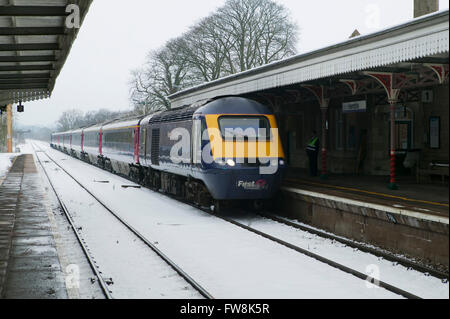 Binari del treno la voce off a distanza con un treno intercity su entrambi appena lasciato o appena arrivati in corrispondenza di una stazione in Cotswolds NEL REGNO UNITO. La Great Western linea di treni è stato ricoperto in una coltre di neve e neve sulle piste e condizioni di congelamento con il ghiaccio in questa scena invernale NEL REGNO UNITO, fanno di viaggio condizioni difficili per il motore. Foto Stock