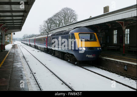 Binari del treno la voce off a distanza con un treno intercity su entrambi appena lasciato o appena arrivati in corrispondenza di una stazione in Cotswolds NEL REGNO UNITO. La Great Western linea di treni è stato ricoperto in una coltre di neve e neve sulle piste e condizioni di congelamento con il ghiaccio in questa scena invernale NEL REGNO UNITO, fanno di viaggio condizioni difficili per il motore. Foto Stock