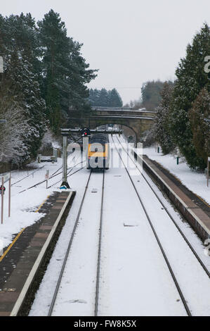 Binari del treno la voce off a distanza con un treno intercity su entrambi appena lasciato o appena arrivati in corrispondenza di una stazione in Cotswolds NEL REGNO UNITO. La Great Western linea di treni è stato ricoperto in una coltre di neve e neve sulle piste e condizioni di congelamento con il ghiaccio in questa scena invernale NEL REGNO UNITO, fanno di viaggio condizioni difficili per il motore. Foto Stock