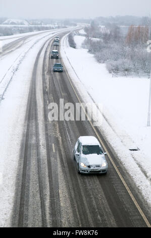 Una vista della A419 / A417 by pass la coperta di neve con i veicoli che viaggiano molto lentamente nella pericolosa condizioni stradali, nella foto dopo un pesante nevicata invernale la strada che teste attraverso il cuore di Cotswolds nel Regno Unito è a malapena praticabile in questi unusally cattive condizioni per viaggiare. Foto Stock