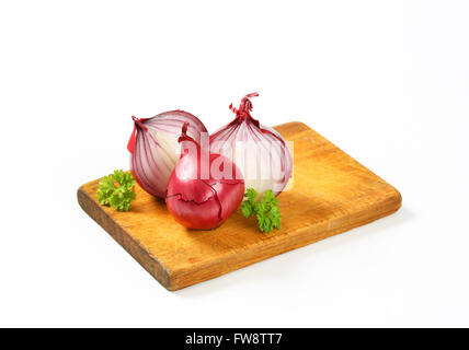 Intero e dimezzato le cipolle rosse sul tagliere di legno Foto Stock