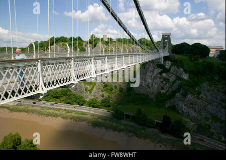 Un uomo attraversare a piedi per il sentiero che corre lungo il lato del ponte sospeso di Clifton, Clifton, Bristol, Regno Unito. Costruito acquistare il famoso ingegnere civile Isambard Kingdom Brunel il ponte attraversa il fiume Avon alcuni 220 piedi sotto l'adn è visto qui in ombra profonda su un lato e del sole sull'altro Foto Stock