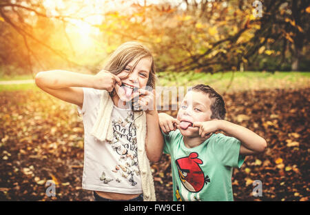 Due bambini che giocano nel parco di autunno facendo facce buffe Foto Stock