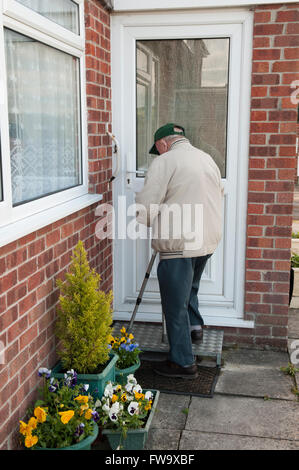 Vista posteriore di un uomo anziano apertura porta anteriore alla sua casa, utilizzando un tappetino anti-scivolo per esterno semi-passo le scale per salire Foto Stock