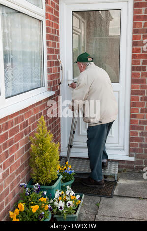 Vista posteriore di un uomo anziano apertura porta anteriore alla sua casa, utilizzando un tappetino anti-scivolo per esterno semi-passo le scale per salire Foto Stock