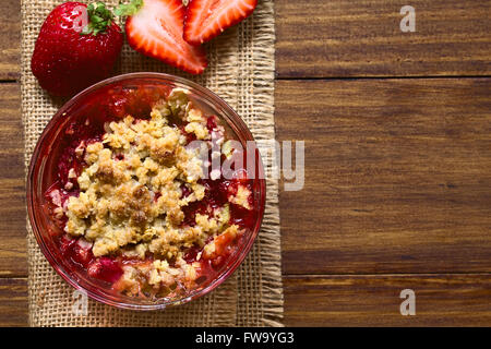 Cotta di fragole e rabarbaro sgretolarsi in recipiente di vetro, fotografato overhead sul legno scuro con luce naturale Foto Stock