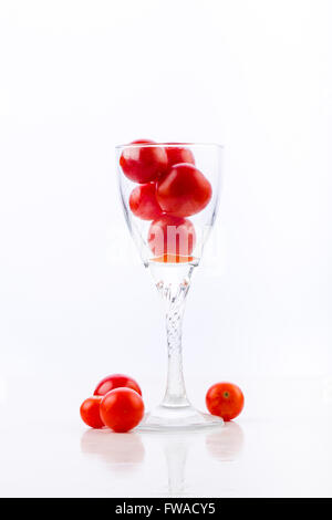 Il succo di pomodoro è versata in un bicchiere con pomodori ciliegia su uno sfondo bianco con la riflessione, bibita salutare per i gourmet Foto Stock