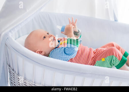 Funny baby in pigiami colorati con bottiglia di bere acqua o latte in bianco presepe con tettoia. Una sana alimentazione per i bambini. Foto Stock