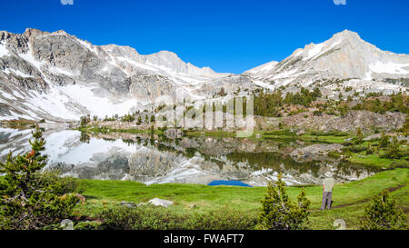 Escursionista guarda con picchi si riflette nel lago a 20 Laghi Bacino della Sierra orientale nel nord della California Foto Stock