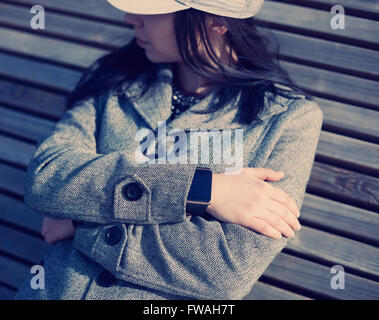 Donna in cappotto grigio weating smart elegante orologio da polso. Questa persona è sempre collegato al social media e internet. La tecnologia moderna e vintage hipster tonificante della pellicola Foto Stock