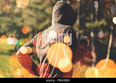 Irriconoscibile uomo incappucciato jogging all'aperto, uno stile di vita sano attività nel parco di inizio autunno mattina, dai toni rétro immagine Foto Stock
