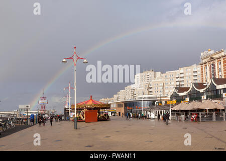 La gente a piedi sotto il cielo grigio e rainbow sul viale di Scheveningen in Olanda Foto Stock