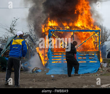 Una baracca prende fuoco e francese di polizia antisommossa della Compagnies Républicaines de sécurité (CRS) utilizzare i loro scudi antisommossa al riparo dai chicchi di grandine durante lo sfratto dei rifugiati e dei migranti a Calais giungla nel nord della Francia. Dotato di: Vista Dove: C Foto Stock