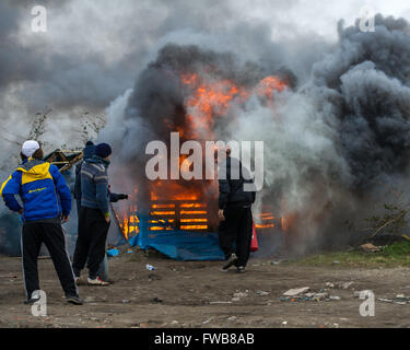 Una baracca prende fuoco e francese di polizia antisommossa della Compagnies Républicaines de sécurité (CRS) utilizzare i loro scudi antisommossa al riparo dai chicchi di grandine durante lo sfratto dei rifugiati e dei migranti a Calais giungla nel nord della Francia. Dotato di: Vista Dove: C Foto Stock