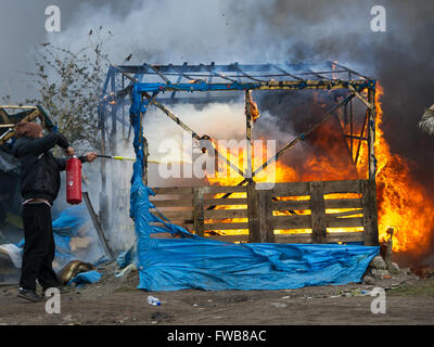 Una baracca prende fuoco e francese di polizia antisommossa della Compagnies Républicaines de sécurité (CRS) utilizzare i loro scudi antisommossa al riparo dai chicchi di grandine durante lo sfratto dei rifugiati e dei migranti a Calais giungla nel nord della Francia. Dotato di: Vista Dove: C Foto Stock