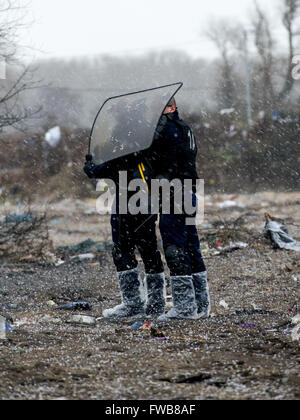 Una baracca prende fuoco e francese di polizia antisommossa della Compagnies Républicaines de sécurité (CRS) utilizzare i loro scudi antisommossa al riparo dai chicchi di grandine durante lo sfratto dei rifugiati e dei migranti a Calais giungla nel nord della Francia. Dotato di: Vista Dove: C Foto Stock