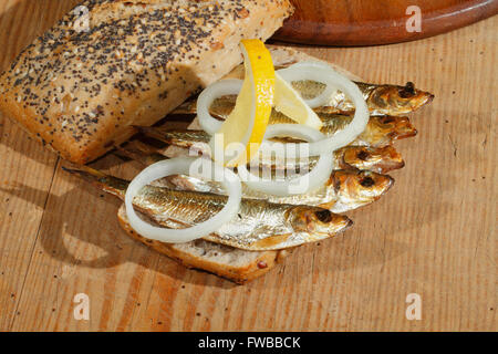 Lo spratto affumicato, guarnita con anelli di cipolla e una fetta di limone in tutto il pane di frumento, con lattuga su un tagliere di legno Foto Stock