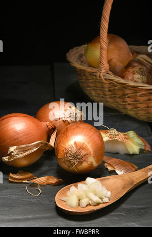 Primo piano di un gruppo di cipolle dorate al buio su un superficie di ardesia. Formato verticale con copia spazio. Foto Stock