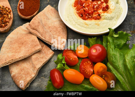 Vista dall'alto di una ciotola di edamame hummus e pita cunei su una superficie di ardesia. Foglia di lattuga, pomodori, spezie e riempire la scena. Foto Stock