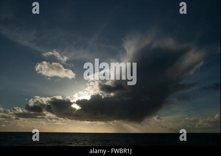 Un enorme nube fuori per vedere nasconde il sole che splende attraverso il squall creazione di un contorno di cloud e evidenziando la consistenza della superficie del mare così come illuminare la zona circostante. Foto Stock