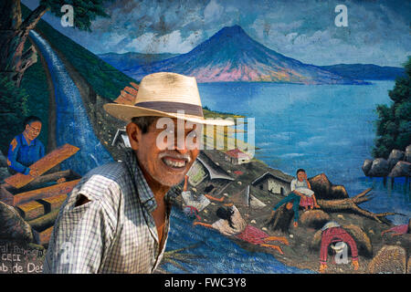 Local uomo a camminare di fronte a un muro dipinto in San Juan La Laguna, Sololá, Guatemala. Maya tradizionale arte pittorica a Santiago Foto Stock