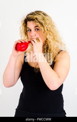 Unica femmina adulta che soffia su di medie dimensioni palloncino rosso Foto Stock