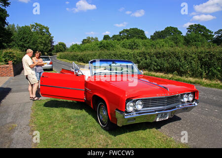 L uomo e la donna in piedi accanto a un rosso convertibili Oldsmobile American classic car in un paese di lingua inglese lane Foto Stock