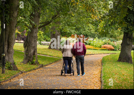 Giardini della valle, Harrogate, nello Yorkshire, Inghilterra - Vista posteriore della giovane coppia (con passeggino) camminando su un viale alberato in questo bellissimo e tranquillo parco. Foto Stock