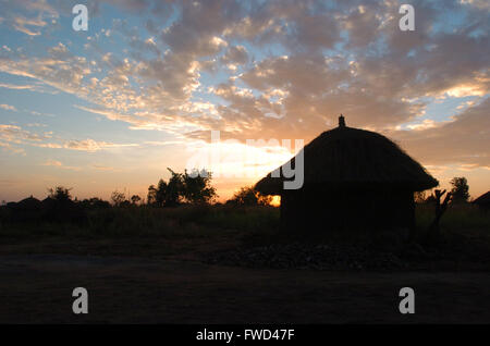 Lacekocot, distretto di Pader, Uganda. 2009. La sun red imposta oltre il paesaggio di capanne di fango e palme al Lacekocot sfollati interni nel campo di Pader, Uganda settentrionale. Foto Stock