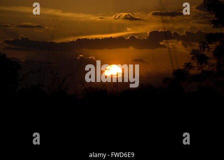 Lacekocot, distretto di Pader, Uganda. 2009. La sun red imposta oltre il paesaggio di capanne di fango e palme al Lacekocot sfollati interni nel campo di Pader, Uganda settentrionale. Foto Stock