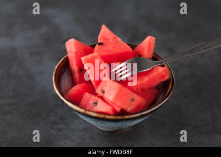 Fette di anguria in ceeramic ciotola con forcella sul grungy scuro dello sfondo. Profondità di campo. Foto Stock