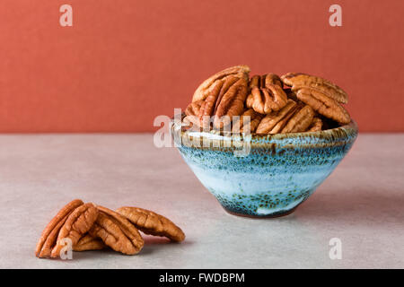 Le noci pecan sulla superficie di marmo e nel vaso di ceramica con sfondo marrone. Spazio di copia, la profondità di campo Foto Stock